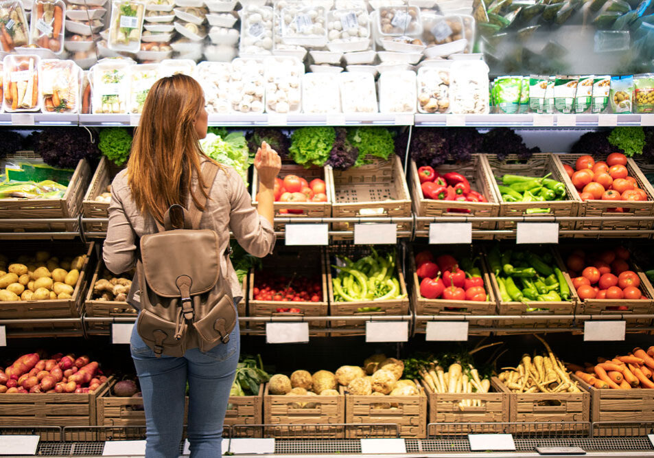 En kvinde står i supermarkedet og kigger på grøntsager. Man ser hende bagfra, og en masse kasser med frugt og grønt. Hun er medlem af Dansk Vegetarisk Forening, så det er selvfølgelig en vegetarret hun skal hjem og lave.